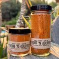 Two jars of Hoot 'N Holler spice on a wooden surface with a blurred outdoor background